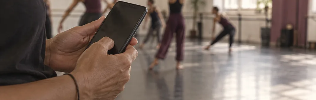 Mão segurando o celular com a lista de presença aberta, turma alongando ao fundo