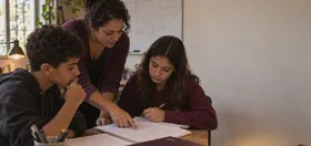 Professora apontando o caderno entre dois adolescentes, lousa com equações ao fundo